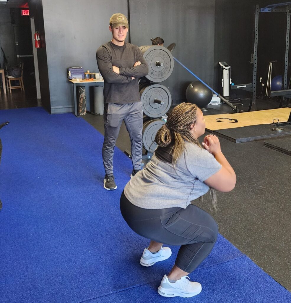 personal trainer checking the form of his client while she squats