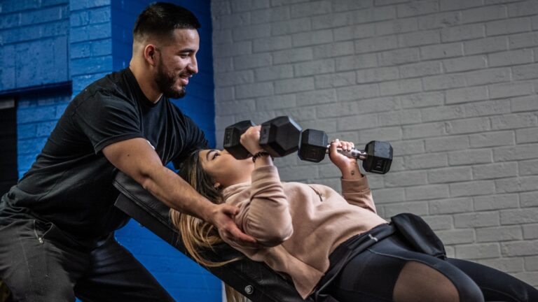 personal trainer assisting his client with a dumbbell incline bench press